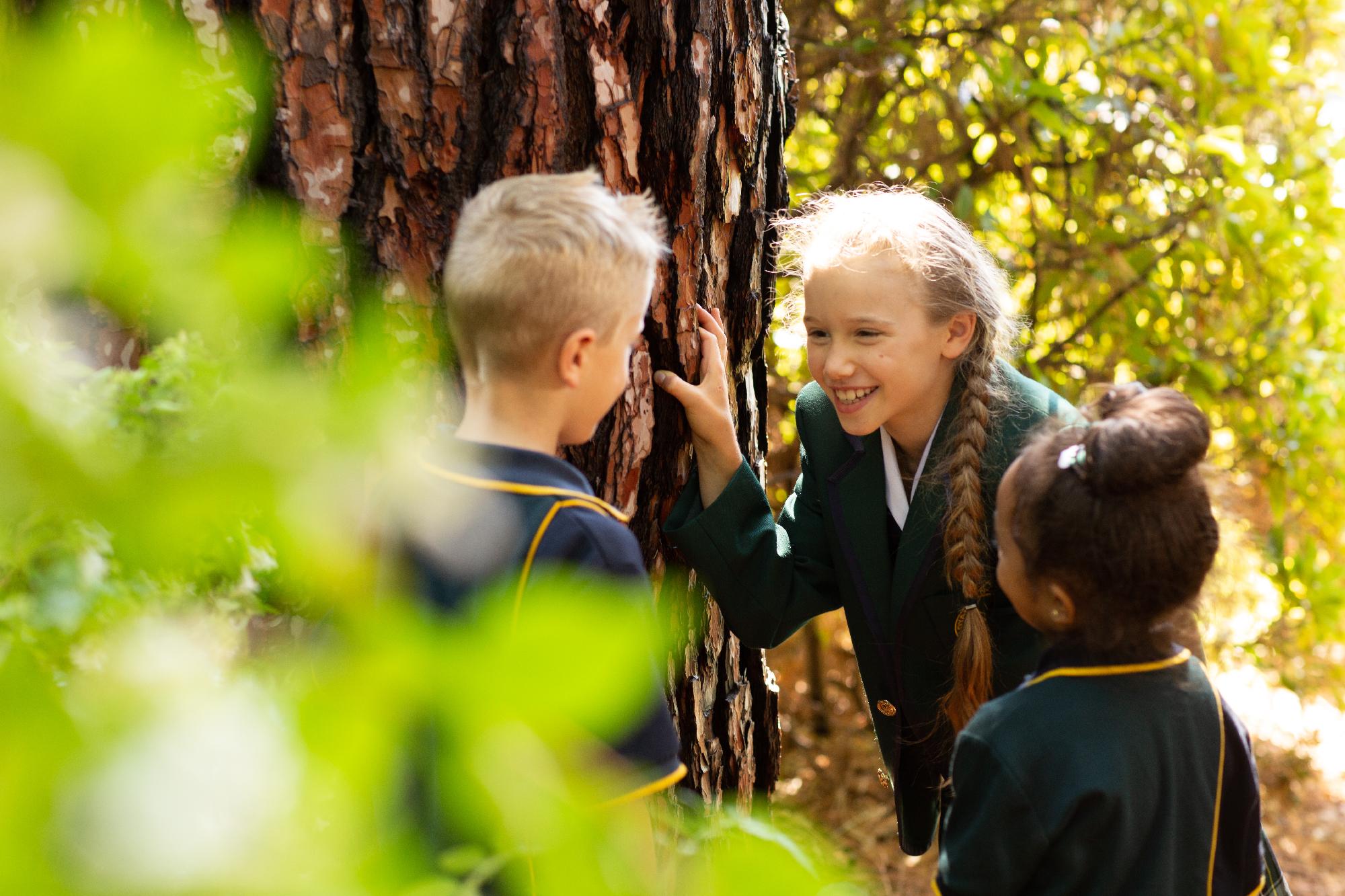 Students at Mercedes College gather around a tree during an outdoor class, with sunlight highlighting their happy expressions.